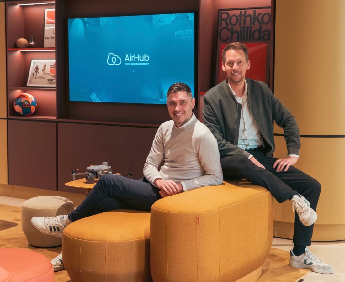 Two AirHub founders seated in front of a screen showing the AirHub Drone Operations Platform, with a drone beside them