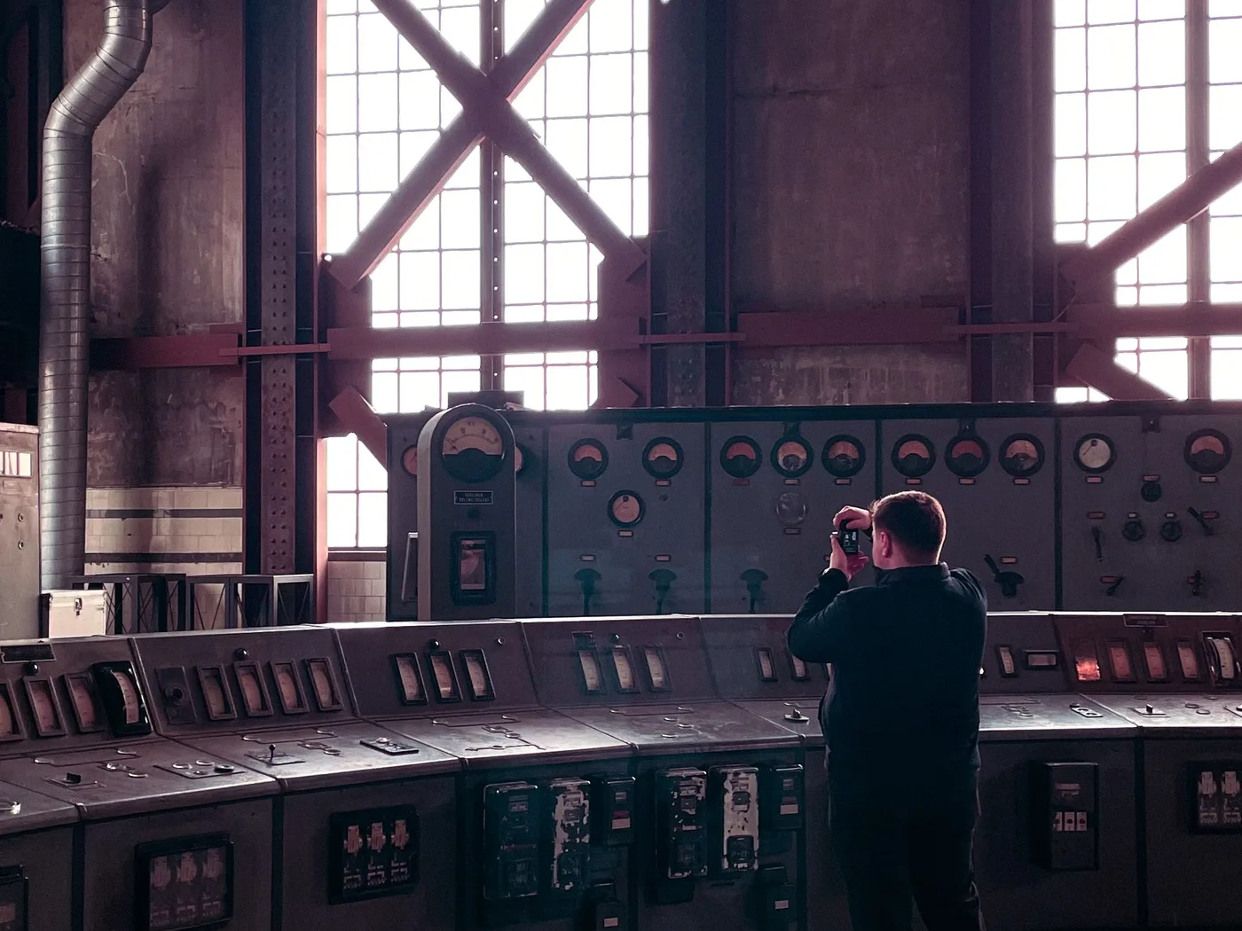 An operator standing at a wall of analogue dials and gauges in an industrial control room