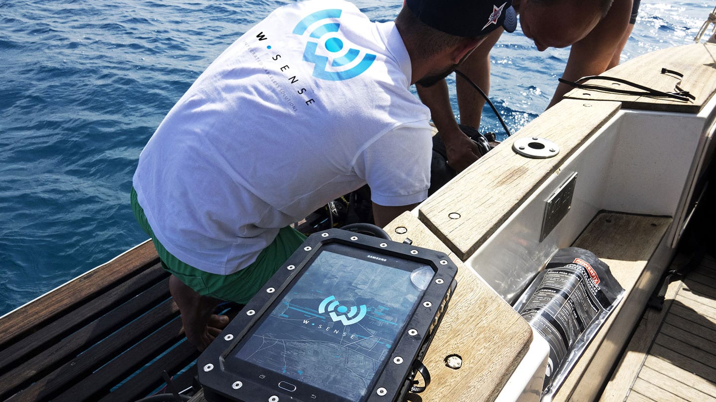 WSense engineers deploying a node from a boat, with a ruggedized tablet running the WSense interface